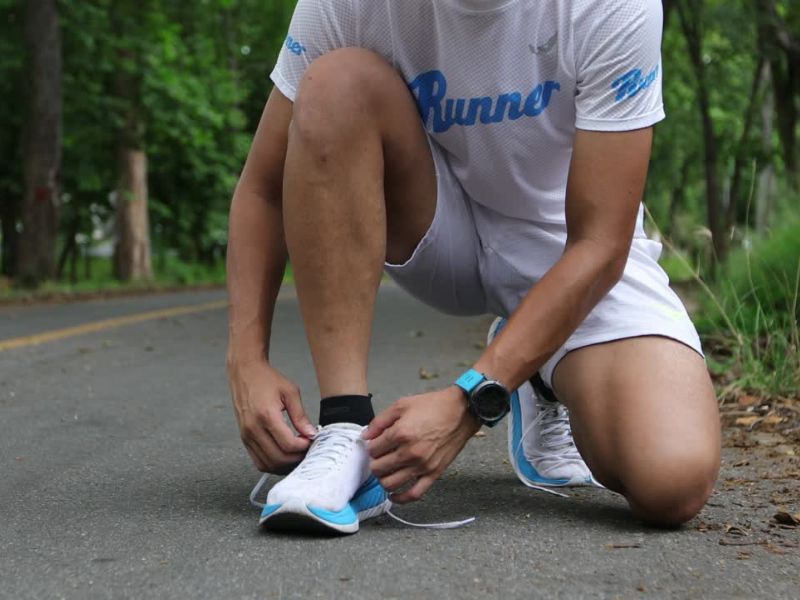 dečko spoprtski obučen kleči i vezuje svoje patike